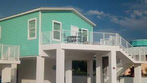 A two-story building with a green exterior and white trim. It features a covered outdoor area with a staircase leading to the upper floor. - New Construction in Venture Out! 3 night minimum stay. (Cudjoe Key)