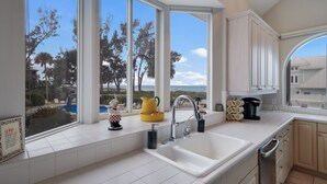 A kitchen with a large window, a sink, and a view of the beach.