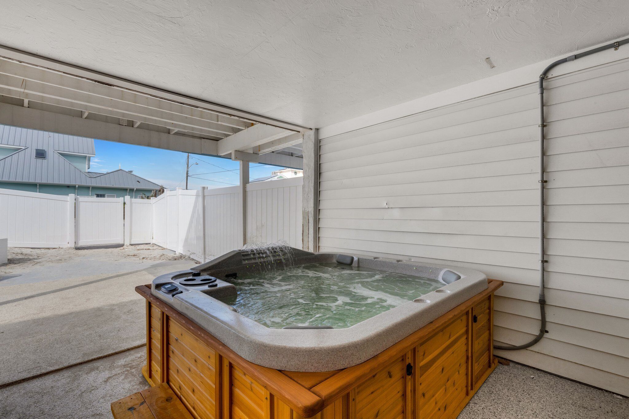 Un bain à remous dans un espace extérieur abrité, avec une porte de garage blanche et une clôture en bois en arrière-plan.