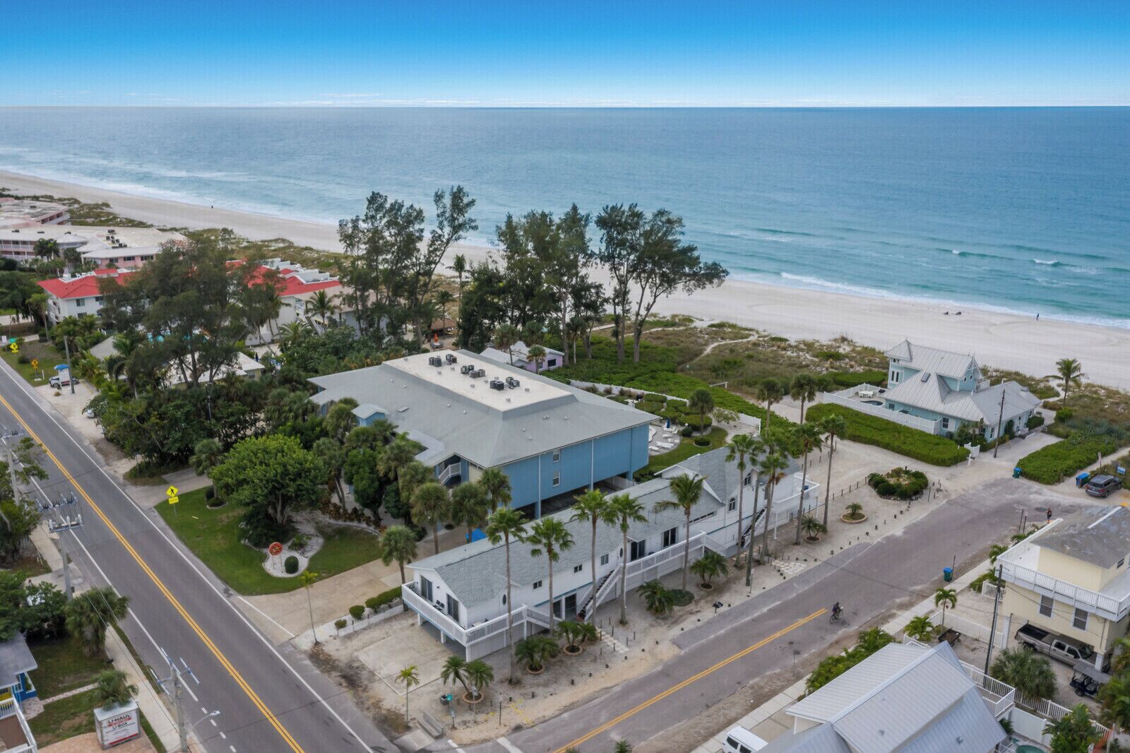 Vista aérea de una propiedad costera con playa, un edificio grande de techo plano y una carretera.