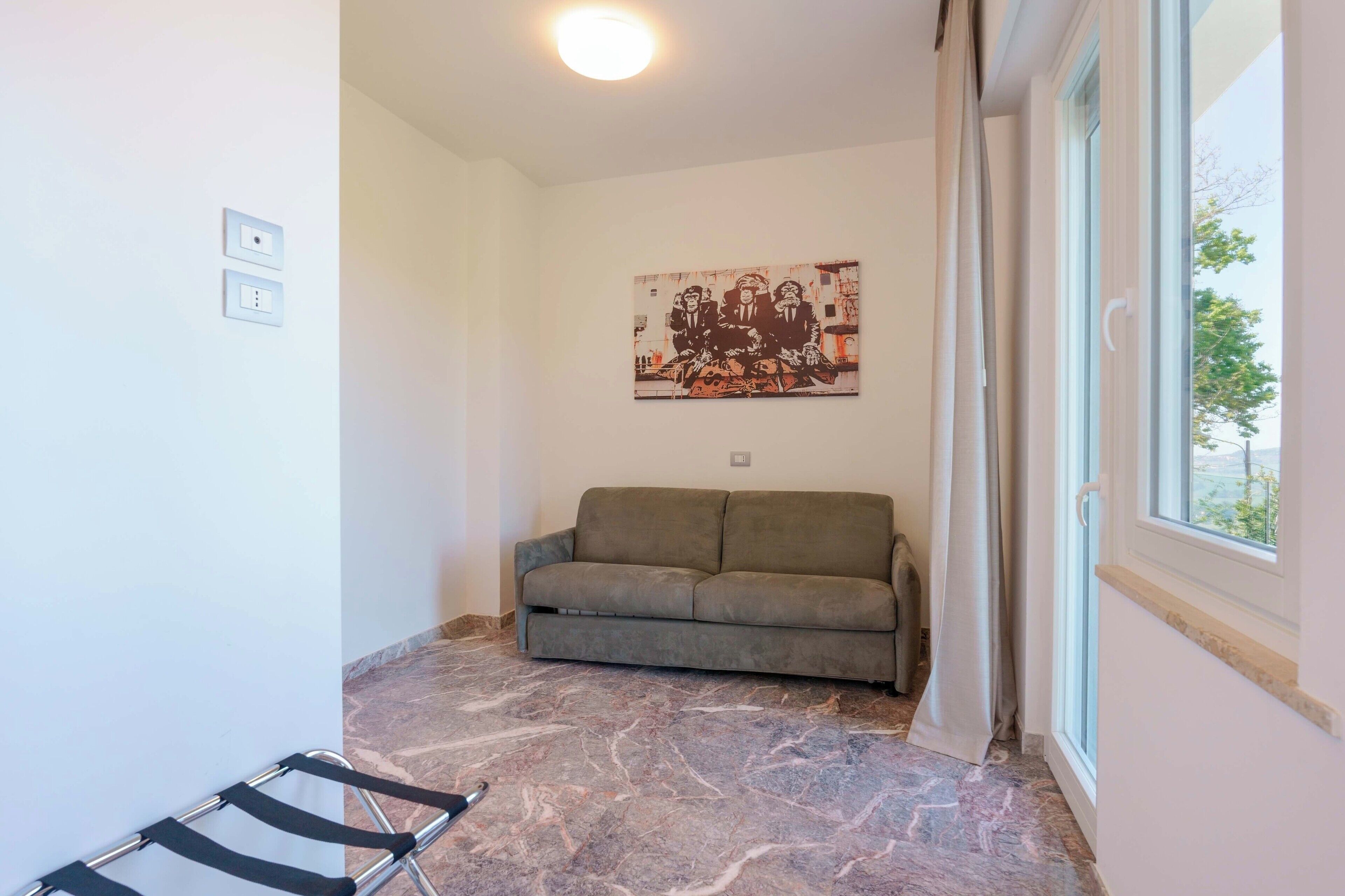 A room with a sofa, a painting on the wall, and a window.