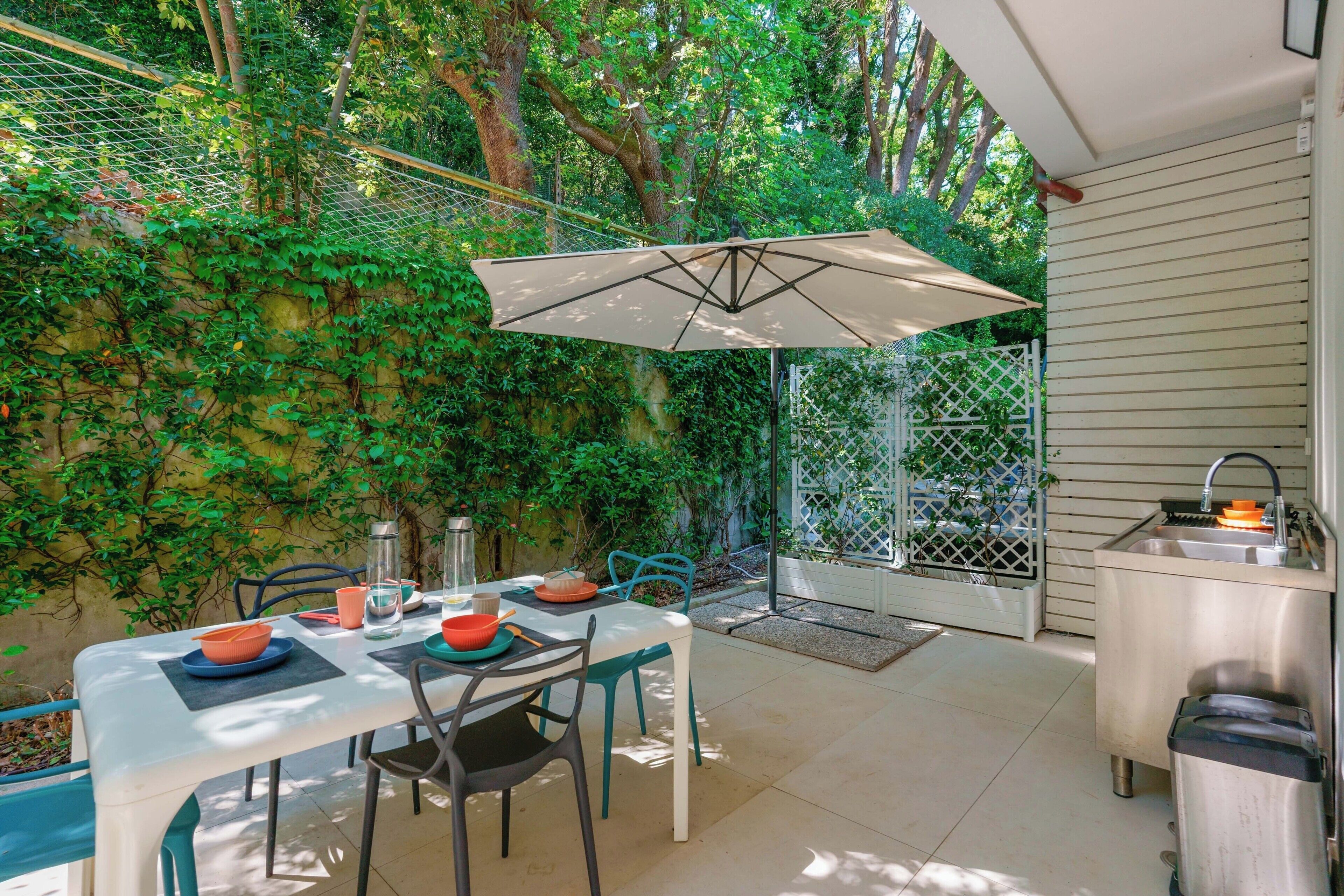 Eine Terrasse im Freien mit Esstisch, umgeben von Grünpflanzen und einem weißen Zaun.