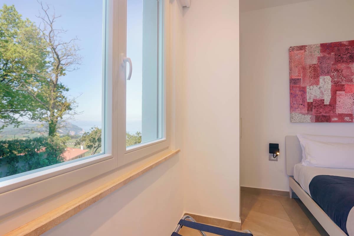 A bedroom with a bed, a window with a view of trees, and a wall-mounted artwork.