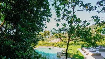 Ein Pool, umgeben von üppigem Grün, einer Holzterrasse und Sitzmöglichkeiten im Freien.