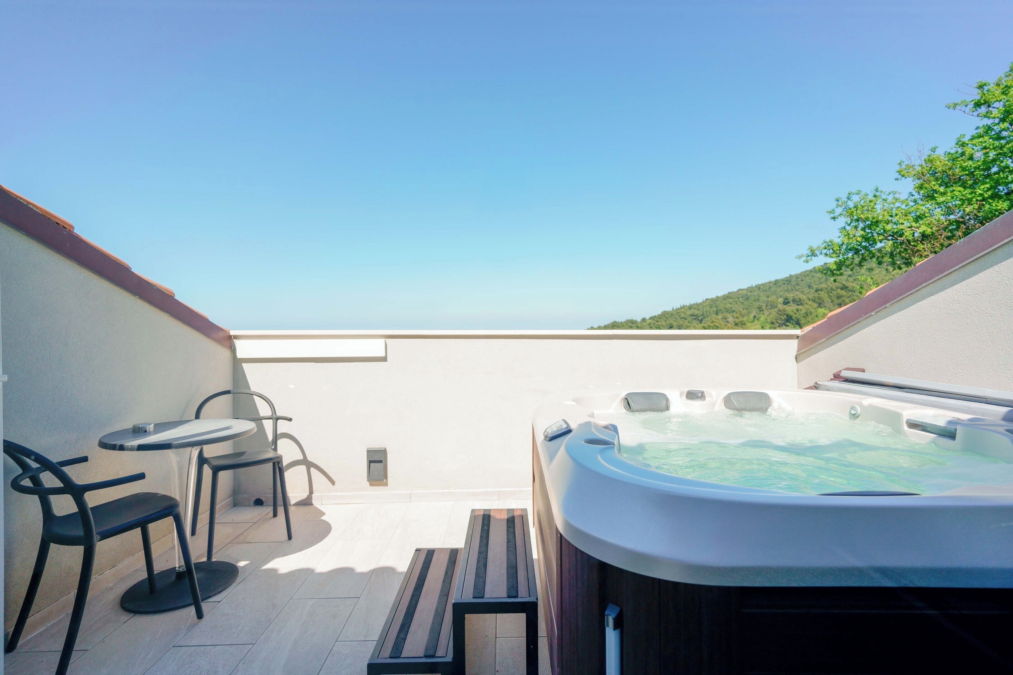 A rooftop terrace with a hot tub, two chairs, and a table.