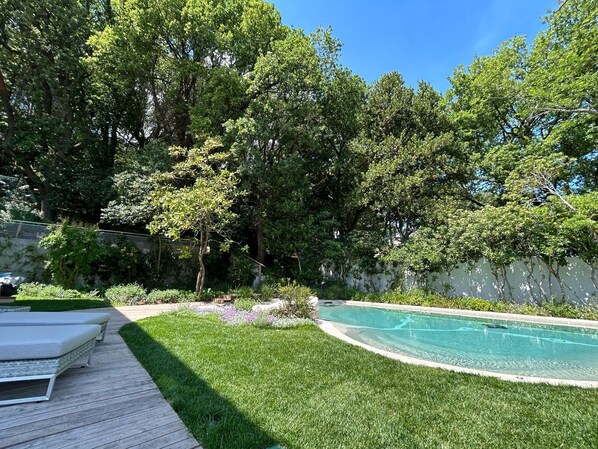 Relax in a serene backyard with a well-maintained lawn, a curved pool, and a deck area surrounded by lush greenery.