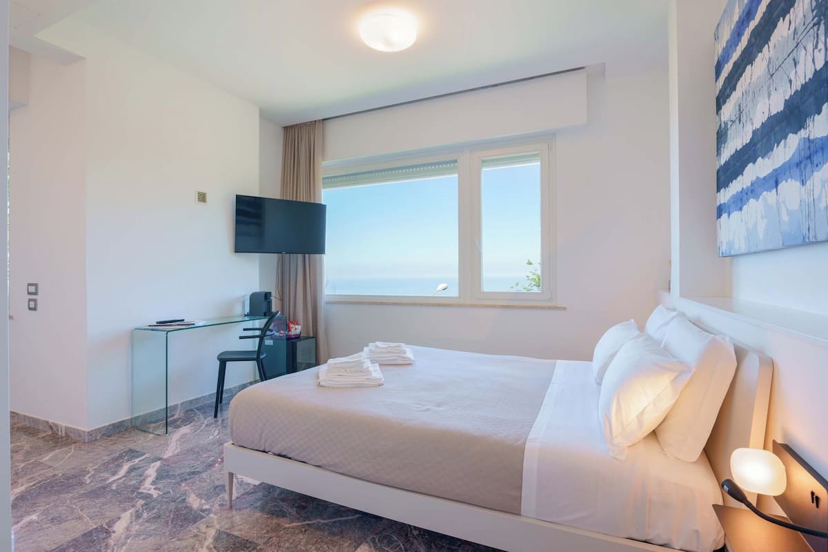A hotel room with a bed, a desk, a TV, and a window with a view.