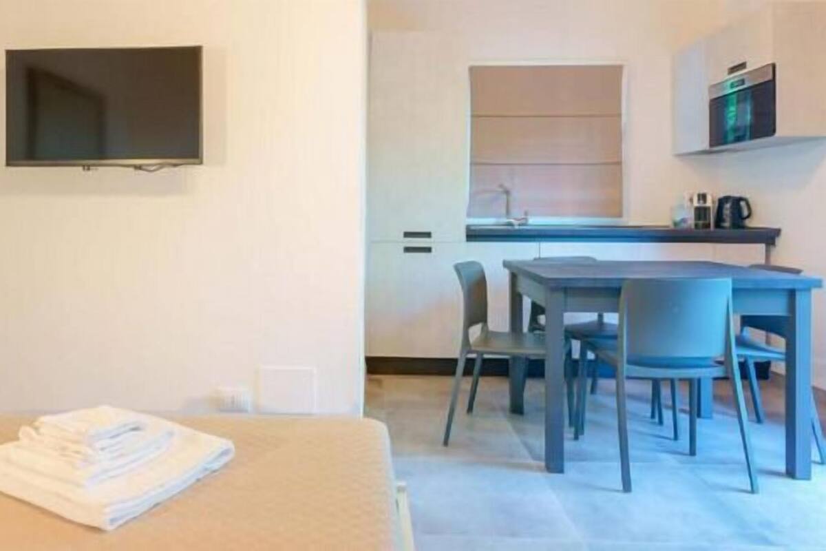 A hotel room with a bed, a desk, a chair, a television, and a kitchenette.