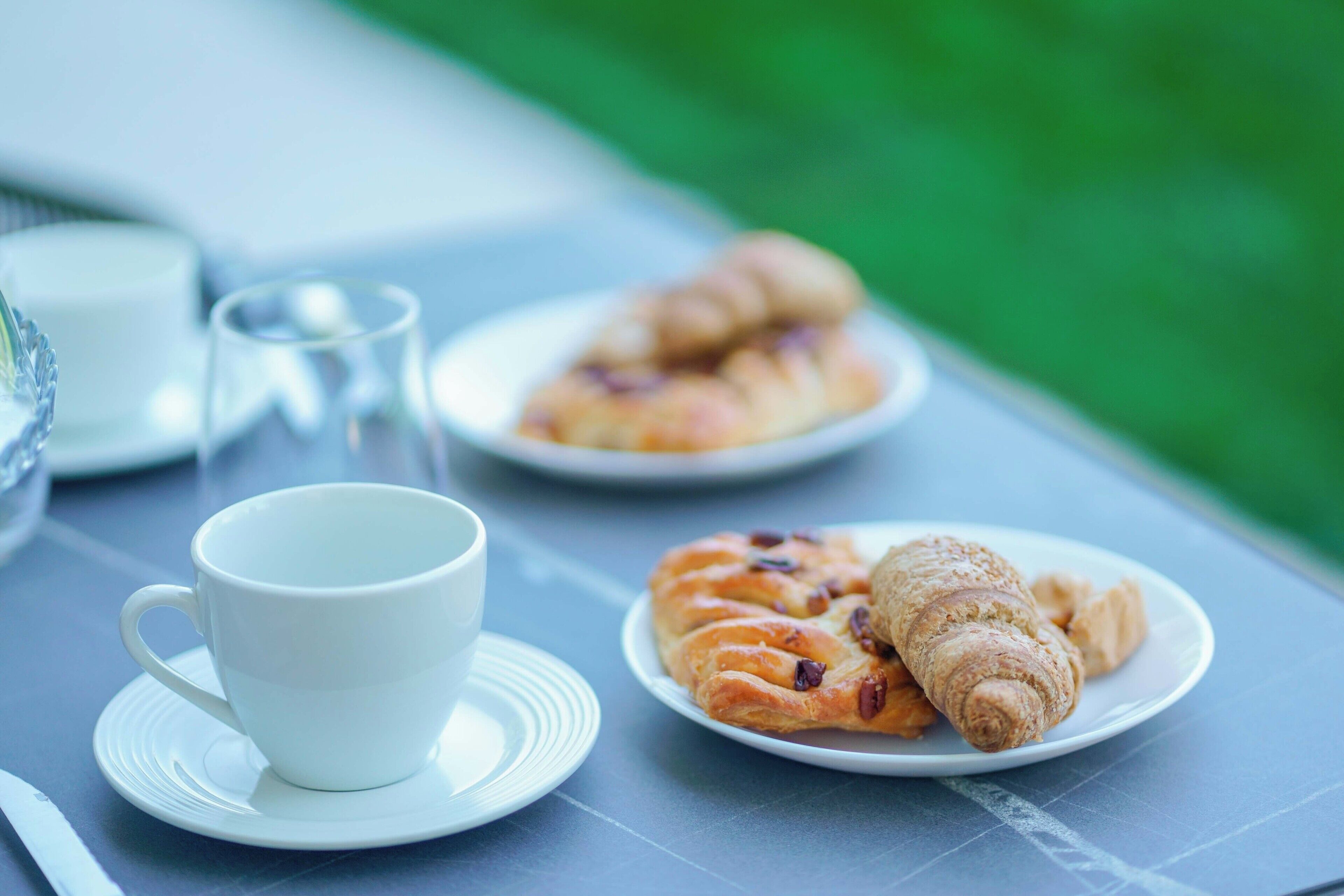 Een tafel met een witte kop, een bord croissants en een glas water.