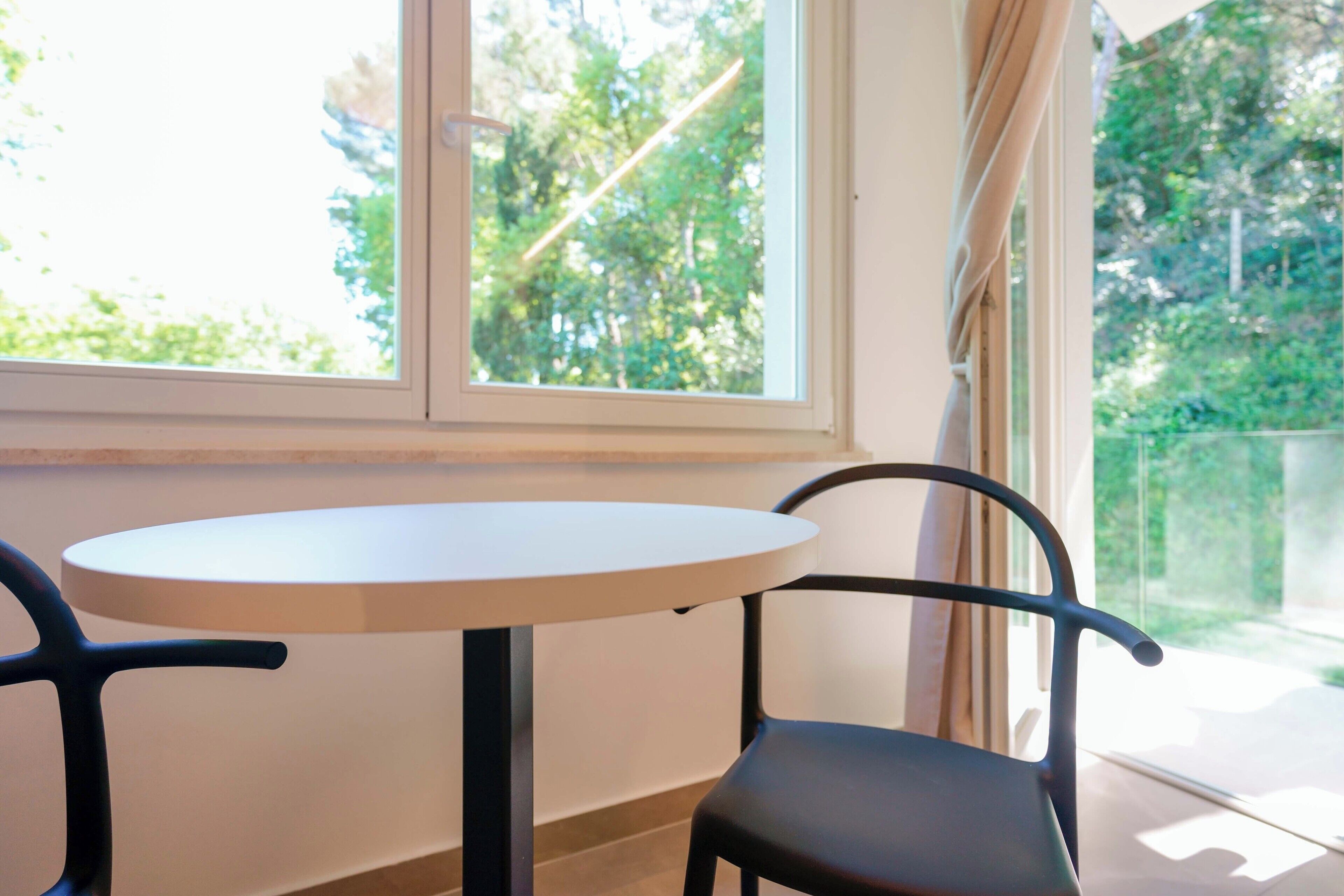Ein runder Tisch mit zwei Stühlen, ein Fenster mit Blick auf Grünflächen und eine Tür.