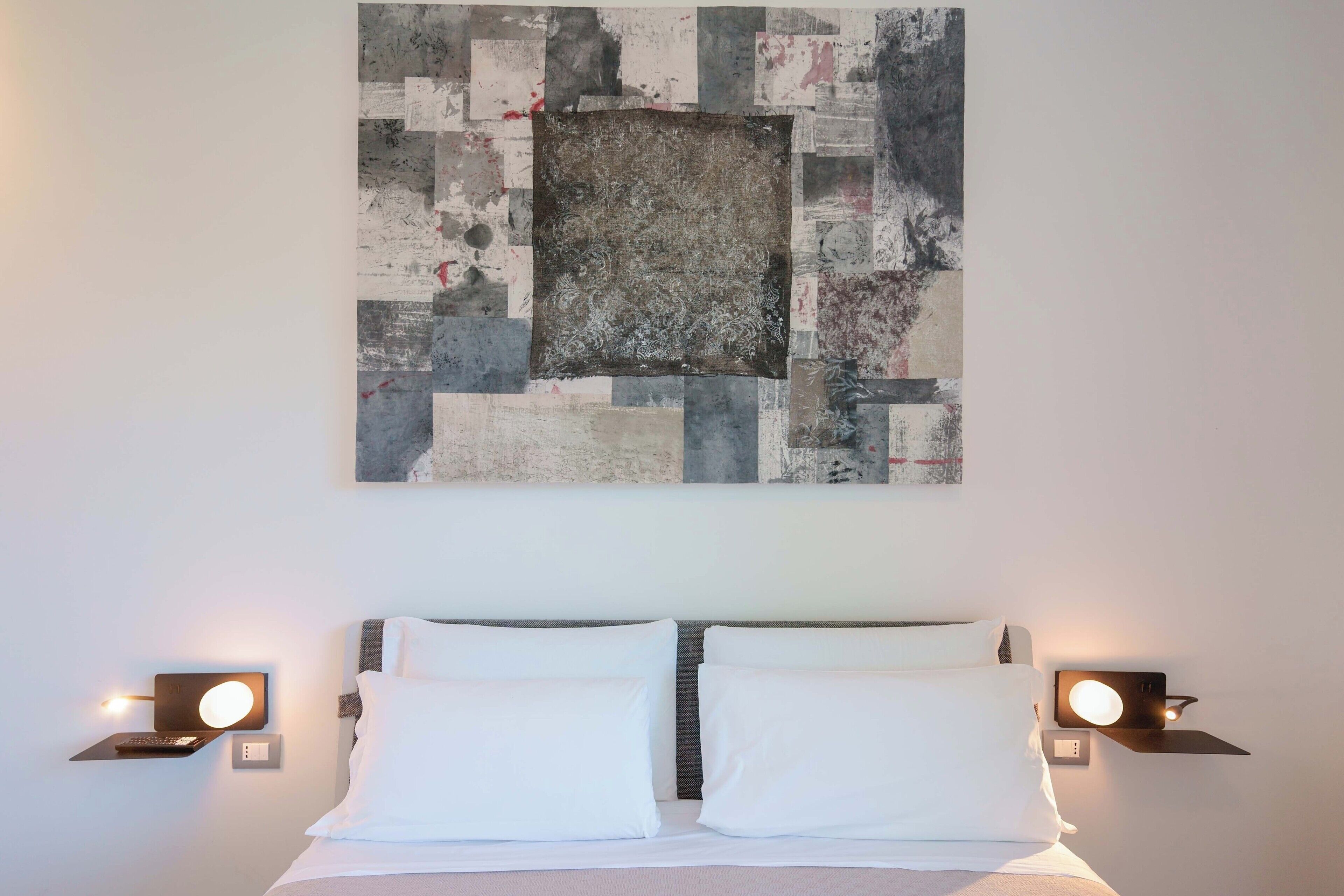 Una habitació d'hotel amb un llit, dues làmpades de nit i una obra d'art abstracta gran a la paret.