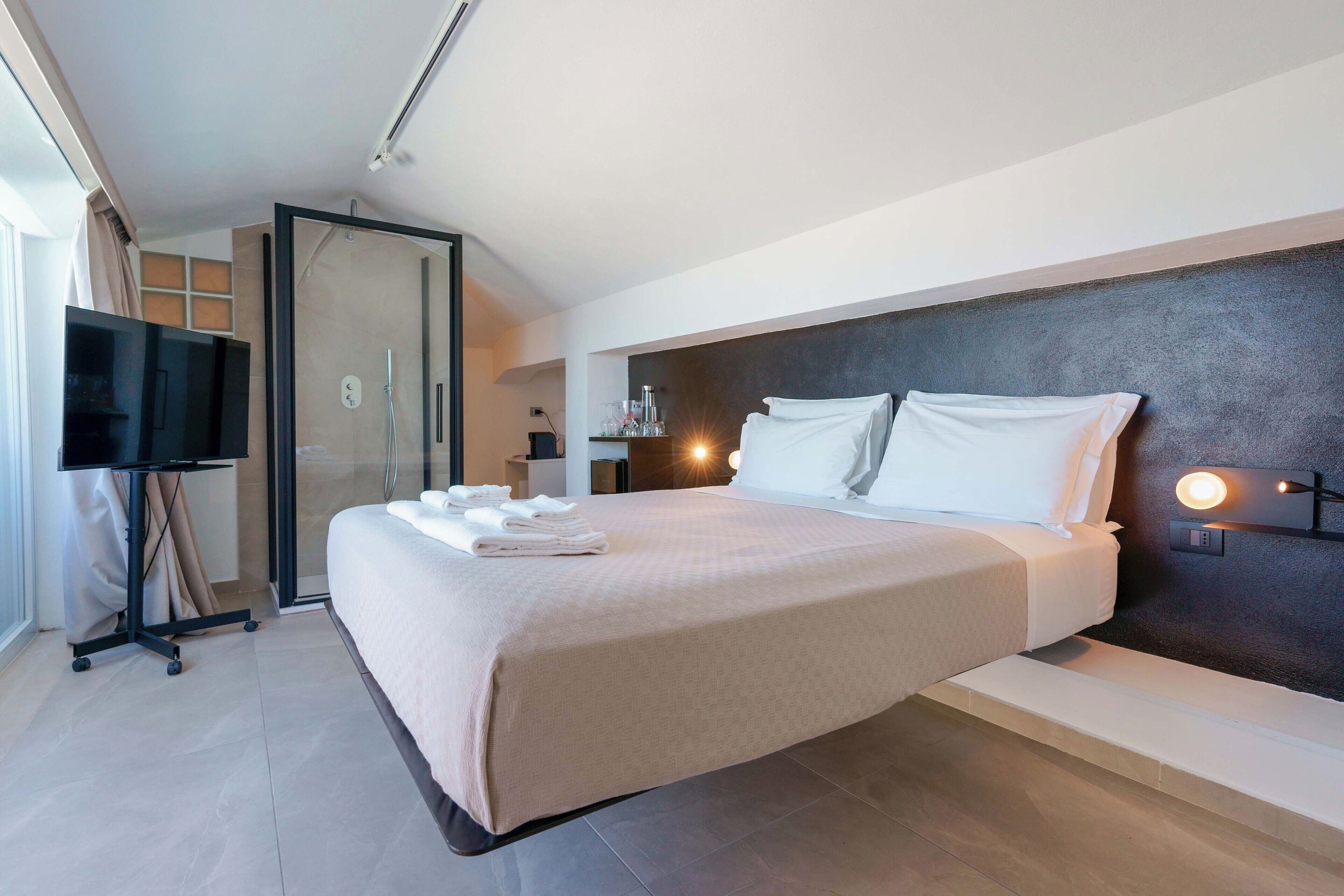 Una habitación de hotel moderna con una cama grande, televisor, escritorio y zona de ducha.