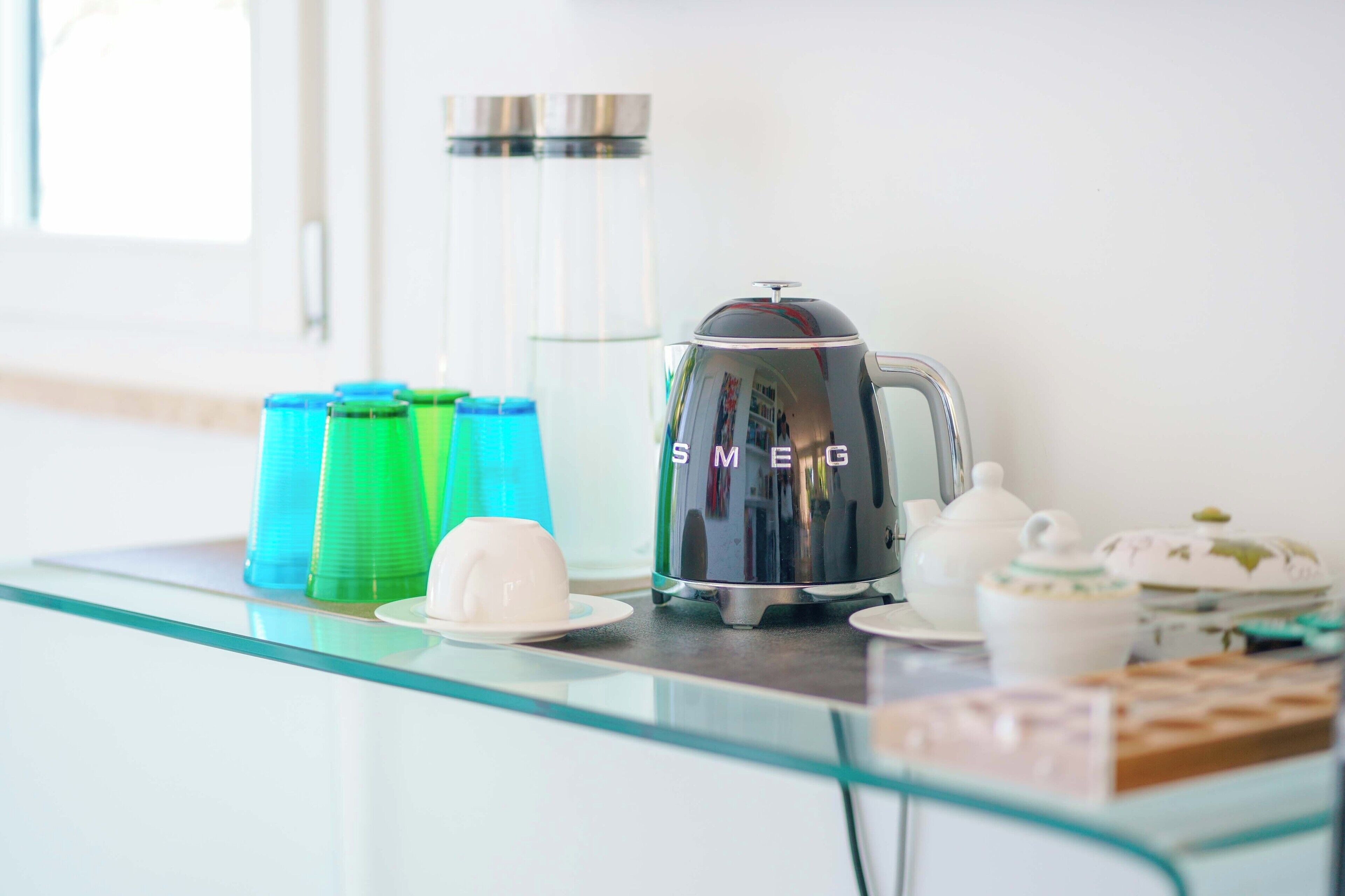 Una encimera de cocina con cafetera, tetera, tazas y dispensador de agua.