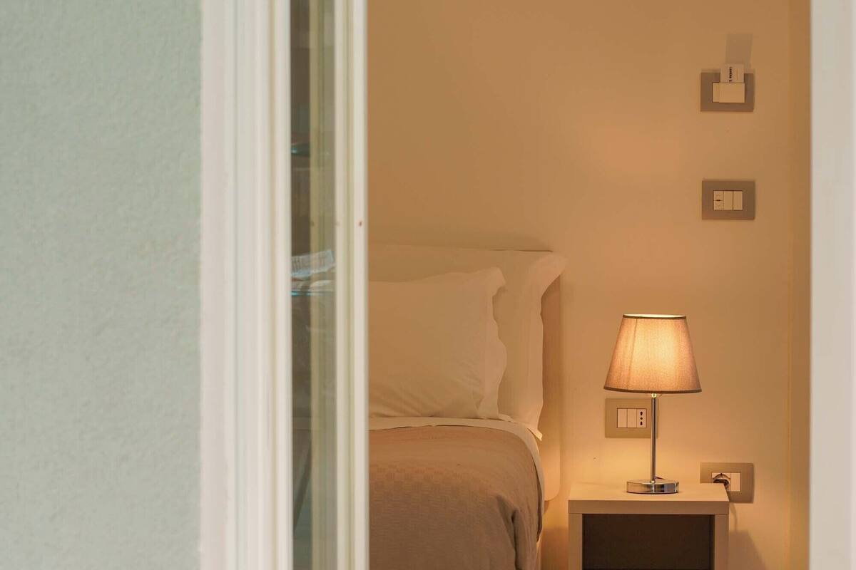 A bedroom with a bed, bedside table, lamp, and a bowl on a table.