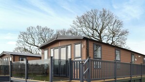 En moderne, toetagers mobilhome med træfacade, store vinduer og en balkon med gelænder af glas.