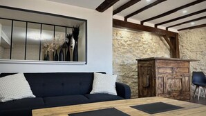Ein Wohnzimmer mit schwarzem Sofa, Holztisch, Steinwand und Holzbalken an der Decke.