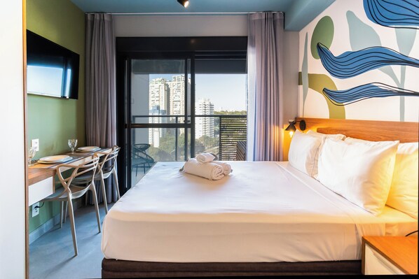 A hotel room with a bed, a desk, and a chair. There is a window with a view of buildings outside. - Haus Residence Brooklin (São Paulo)