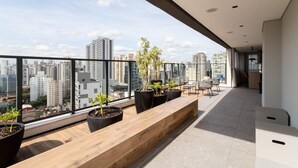 A modern balcony with a city view, potted plants, and a wooden bench. - Haus Residence Brooklin (São Paulo)