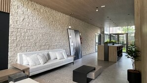 A modern living area with a stone wall, a white sofa, a black coffee table, and a kitchen area in the background. - Haus Residence Brooklin (São Paulo)