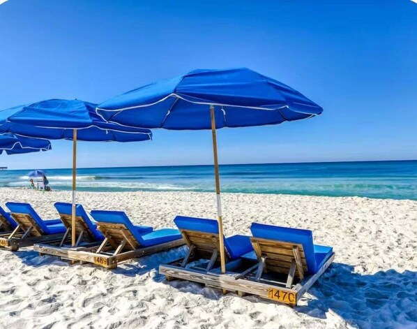 A beach with blue umbrellas and wooden lounge chairs.