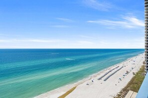 Uma praia com águas turquesa cristalinas, uma extensa faixa de areia e um edifício alto à direita.