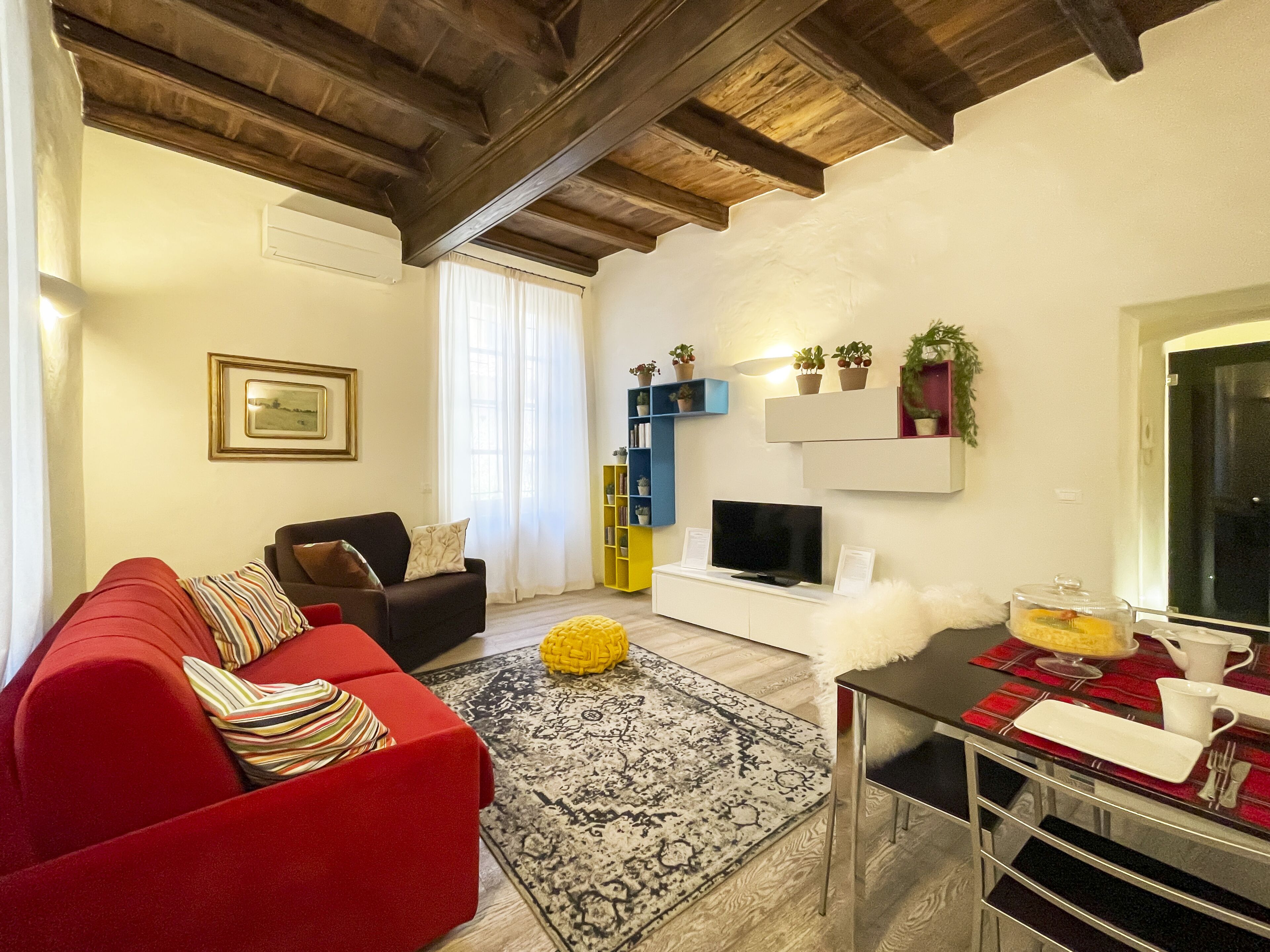Een woonkamer met een rode bank, een televisie en een eethoek met een tafel gedekt voor twee personen.