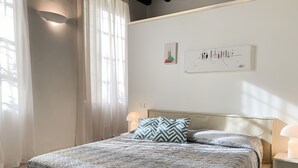 Ein ordentlich gemachtes Bett mit gemusterten Betttextilien, einer Nachttischlampe und zwei Wandbildern.