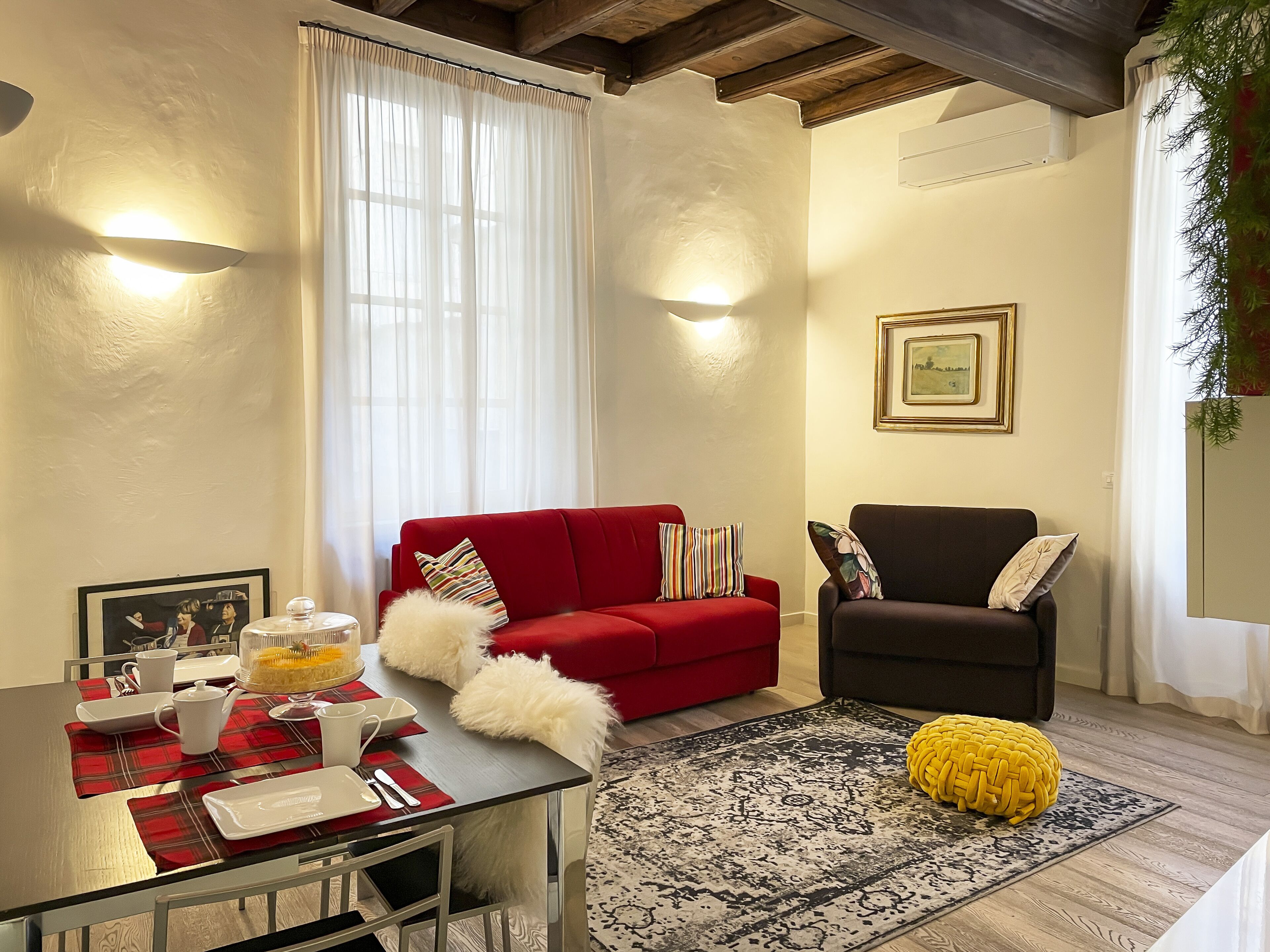 Un salon avec un canapé rouge, un fauteuil noir, une table basse en verre et un tapis à motifs.