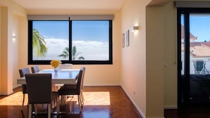 Ein Essbereich mit Tisch und Stühlen, große Fenster mit Blick auf Himmel und Wolken sowie eine Tür, die nach draußen führt.