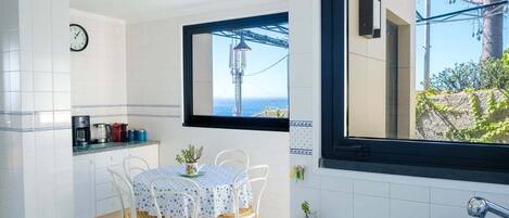 A compact kitchen with a dining area, a clock on the wall, and a view of the sea through a window.