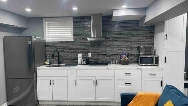 Una cucina moderna con mobili bianchi, frigorifero in acciaio inossidabile, forno a microonde e forno da incasso.
