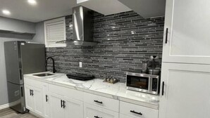 Una cucina moderna con mobili bianchi, un frigorifero in acciaio inossidabile, un forno a microonde e un rivestimento a parete in piastrelle nere.