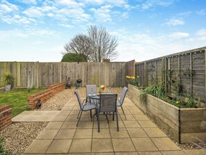 A patio with a table and chairs, a brick planter, and a wooden fence. - 1 bedroom accommodation in Martham (Martham)