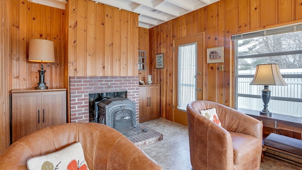 A cozy living room with wooden walls, a fireplace, leather sofas, and a large window. - 1 Mi to Beach! Family Gloucester Gem w/ Yard (Gloucester)