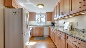 A kitchen with wooden cabinets, a white refrigerator, a granite countertop, and a window. - 1 Mi to Beach! Family Gloucester Gem w/ Yard (Gloucester)