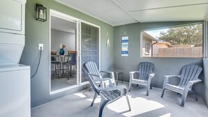 A covered patio area with two Adirondack chairs, a small table, and a view of the backyard through a sliding glass door. - Cocoa Home w/ Large Yard: 3 Mi to Indian River! (Cocoa)