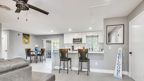 A modern kitchen with white cabinets, a microwave, and a bar area with two stools. - Cocoa Home w/ Large Yard: 3 Mi to Indian River! (Cocoa)