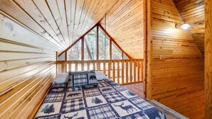 Een houten hutje met een bed, een raam en een houten plafond.