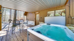 Een houten terras met een jacuzzi, zitplaatsen buiten en uitzicht op het bos.