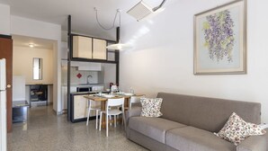 Una sala de estar moderna con un sofá gris, dos sillas blancas, una mesa de comedor y una cocina al fondo.