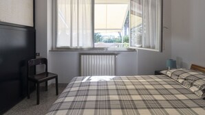 Un dormitorio con cama, una silla, una ventana con cortinas y un radiador.