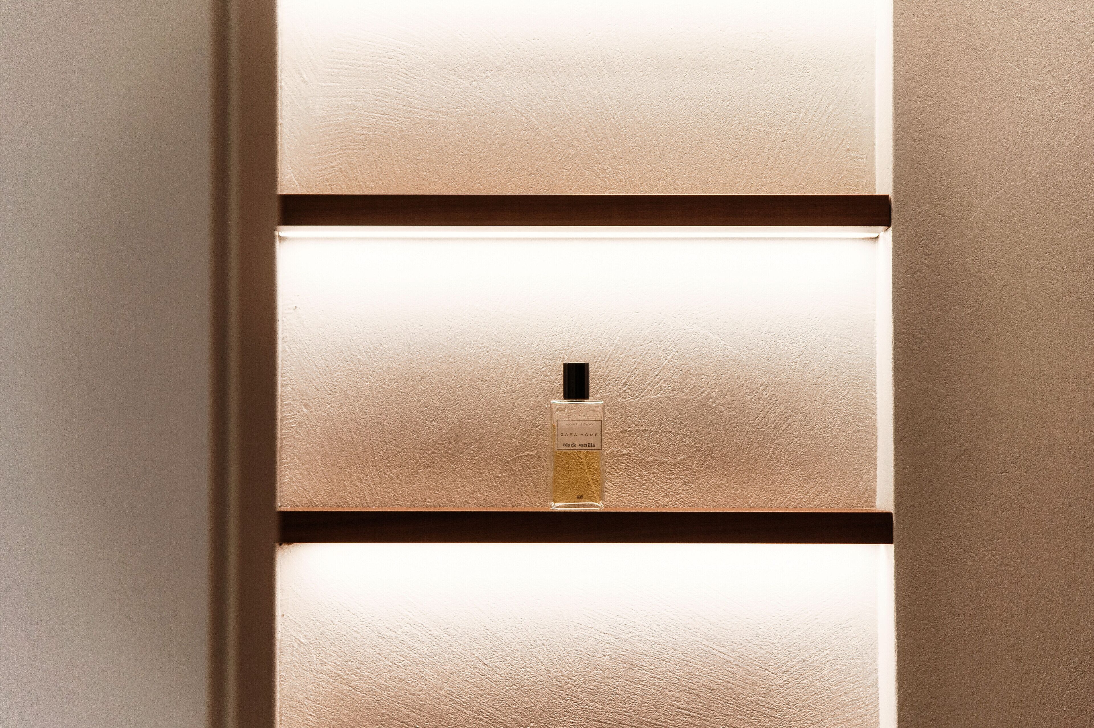 Una botella de perfume sobre una pared texturizada con paneles horizontales.