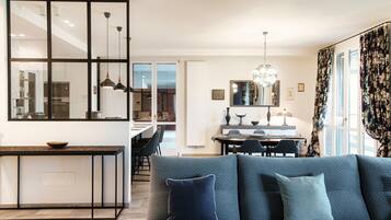 Una sala de estar moderna con un sofá gris, un comedor y una cocina visible a través de un separador de vidrio.