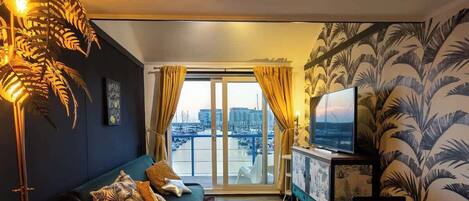 A living room with a sofa, a television, and a view of a marina through large windows.