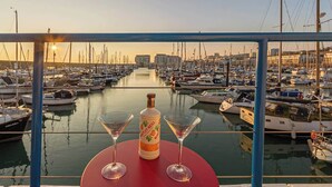 Un port de plaisance avec des bateaux amarrés, une bouteille de spiritueux et deux verres à martini posés sur une table.