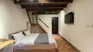 Een slaapkamer met een bed, bureau, stoel, televisie, trap en een deur.