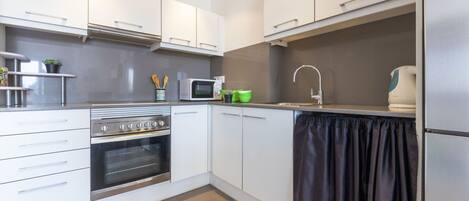 A modern kitchen with white cabinets, a stainless steel oven, a microwave, and a kettle.