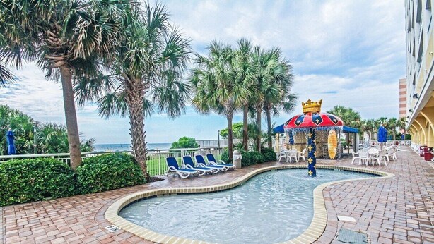 A pool area with lounge chairs, palm trees, and a decorative fountain. - Oceanfront 2Qn Studio. Resort w/Lazy River, Pools (Myrtle Beach)