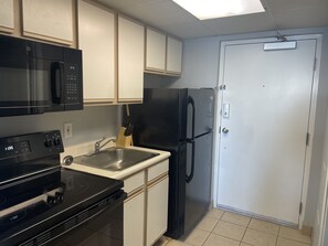 A compact kitchen with a microwave, stove, sink, and black refrigerator.