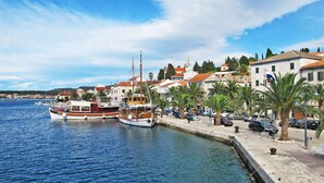 Une ville côtière où des bateaux sont amarrés dans un port de plaisance, où une promenade pavée longe le front de mer, et où l’on trouve des bâtiments traditionnels aux toits recouverts de tuiles rouges.